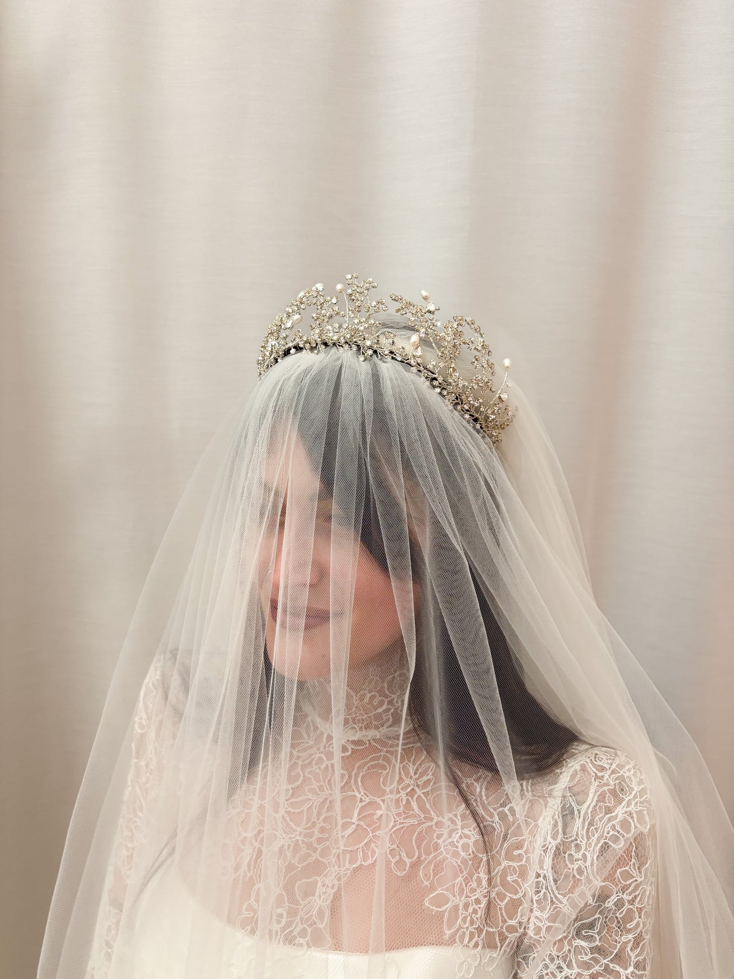 Person wearing a Wuthering Heights Crown and wedding dress with a veil and tiara against a neutral background